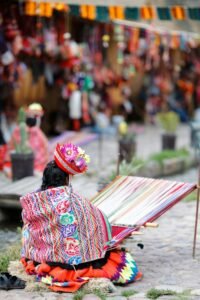 A weaver in traditional outfit crafts textiles in Ollantaytambo, Peru market.
